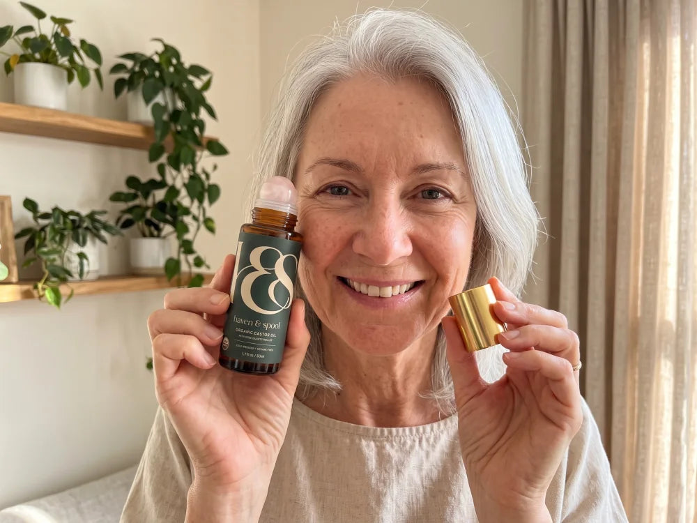 A woman in her sixties at home, smiling, holding the Haven & Spool castor oil roll-on