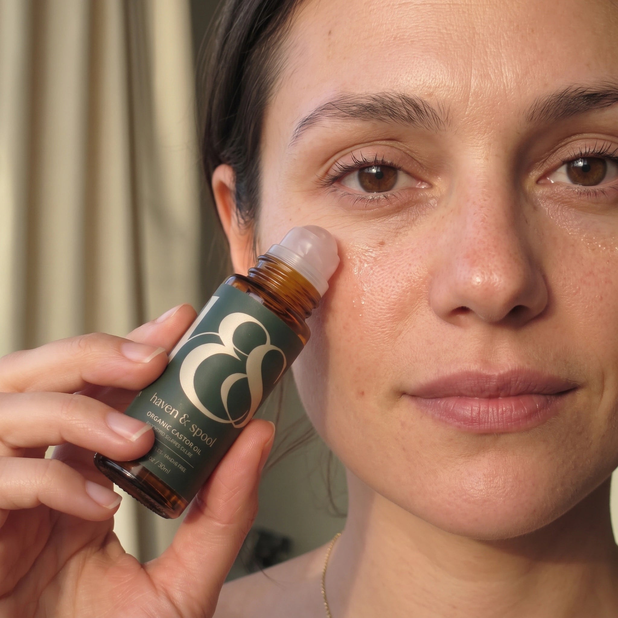 A close-up of a woman rolling the oil under her eye in soft window light