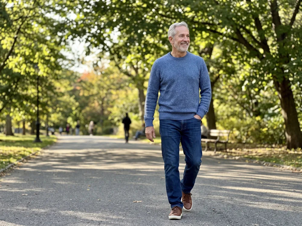 A man in his sixties walking a sunlit park path in the afternoon, smiling, at ease