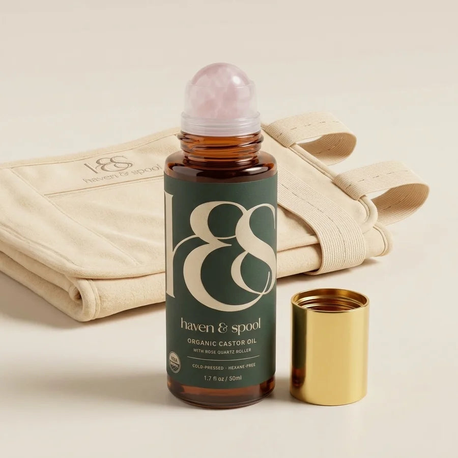 Haven and Spool organic castor oil roll-on with the rose quartz roller, gold cap beside it, and the cotton belly pack folded behind